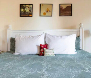 Bed with green blanket and white pillows.